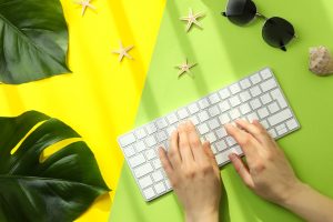 Female hands are typing on the keyboard on color background with vacation accessories